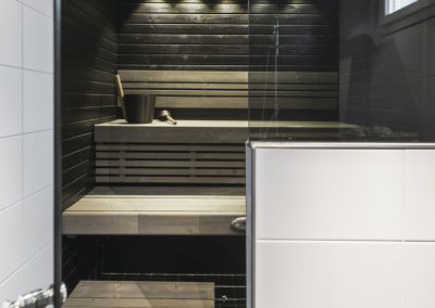 Puolilasiseinällä oleva sauna vaaleilla lauteilla ja mustalla seinäpaneelilla.