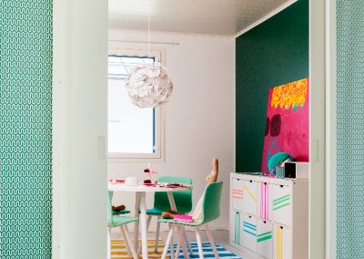 Seinän sisään liukuvat lastenhuoneen pariovet. Huoneessa vihreät tuolit ja tehosteseinä.