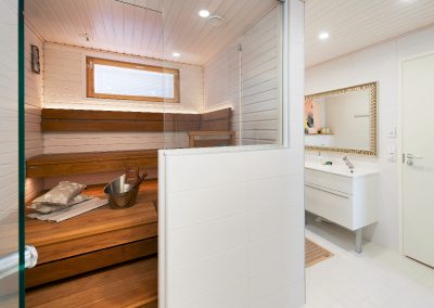 Sauna valkoisella seinäpaneelilla ja puolilasiseinällä.