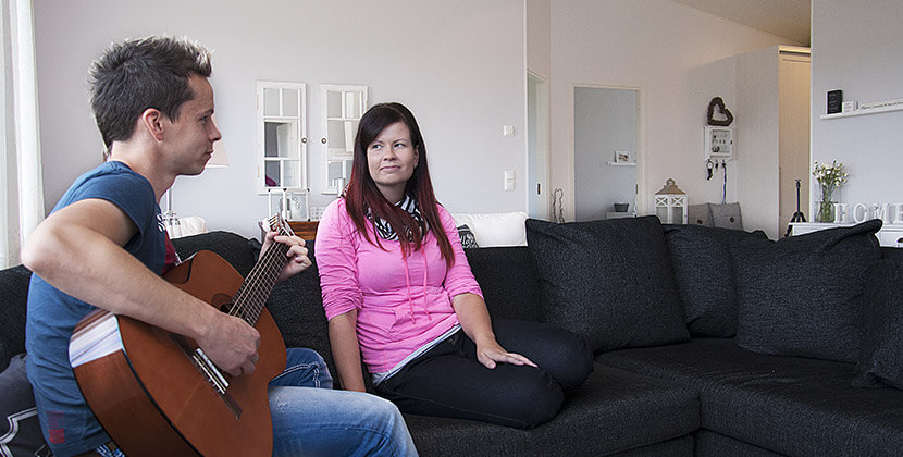 Mies ja nainen istuvat iloisina uuden Dekotalon sohvalla. Mies soittaa kitaraa.