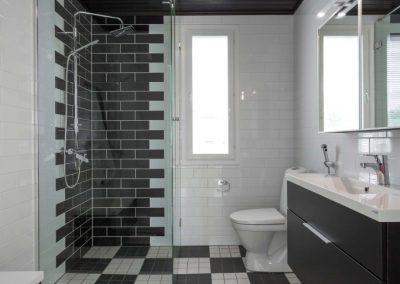 Mustavalkoinen WC/pesuhuone, jossa mustavalkoruutuinen lattialaatoitus ja musta tiililadontainen tehostelaatoitus. Musta kattopaneeli ja kaapiston ovet.