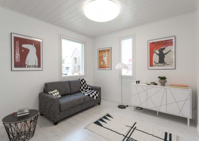 Vaalea huone jossa harmaa sohva, sekä koira-aiheisia tauluja seinällä.