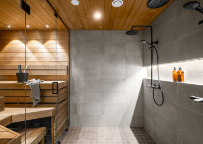 Pesuhuone ja sauna upealla harmaalla laatalla, mustalla suihkulla sekä lasiseinällä saunaan