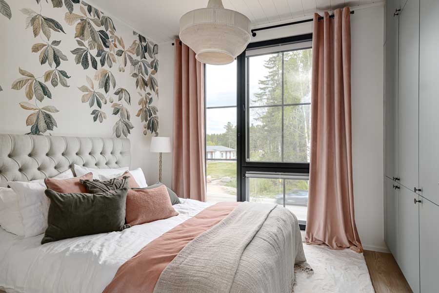 Asuntomessutalo Lilla Hyggen päämakuuhuone, jossa upea kukkatapetti, vangitseva vaaleanpunaiseen taittava värimaailma, Cobellon ylelliset lakanat ja Unikulman laadukas sänky.