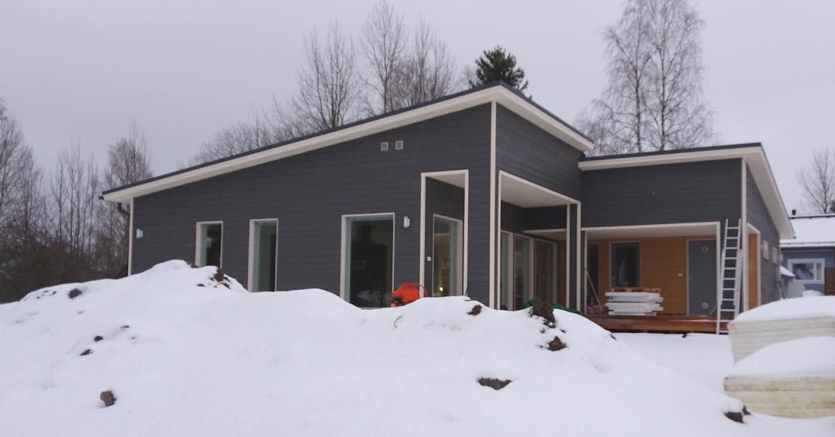 Taloesittelykohteen kuva. L-mallinen talo, tummalla ulkoverhouksella lumisessa maisemassa.