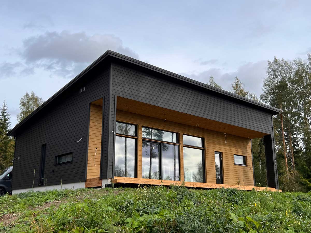 Taloesittelyssä tämä upea Deko 133B muuttovalmis talo. Talo on kuvattu sisäänvedetyn takaterassin suunnasta, jossa on suuret ikkunat suoraan kodin yhteisiin oleskelutiloihin. Musta puuverhous ja kaunis puunsävyn kontrasti terassi osuudessa.